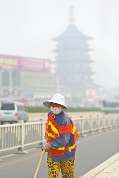 近日，在古都洛陽，環(huán)衛(wèi)工人身后的“天堂”被霧霾籠罩著。