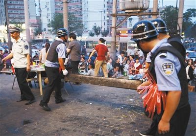 6月13日晚8點(diǎn)，朝陽路和青年路交叉口西側(cè)，一次聯(lián)合執(zhí)法行動(dòng)中，輔警與協(xié)管抬走商戶的燒烤用具。新京報(bào)記者 尹亞飛 攝