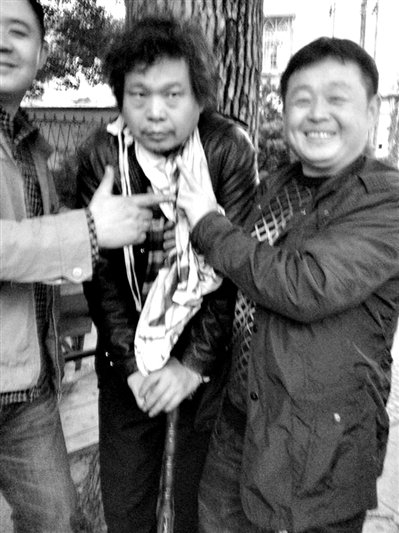 兩名接訪人員與患有癌癥的訪民段新德合影時(shí)，面帶笑容擺出勝利的手勢(shì)。