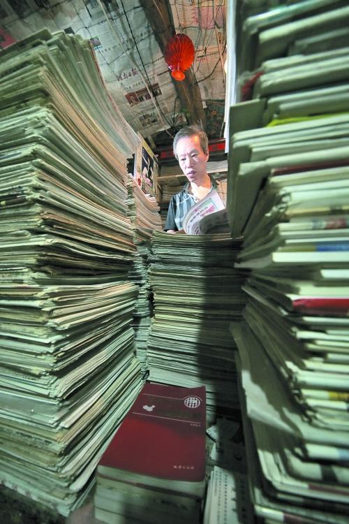 王曉民坐在寫字桌前，被報紙淹沒。