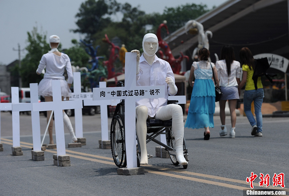 4月16日，重慶市洋人街上擺放著兩個受了傷的塑料人像“模特”，旁邊十字架上寫著向“中國式過馬路”說不