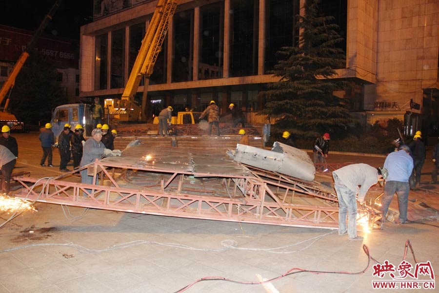 地面上的20多名工人對(duì)吊裝下的廣告牌進(jìn)行分割。