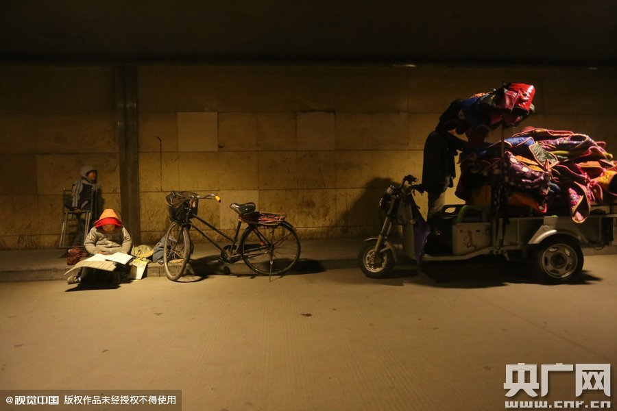 2015年11月8日晚，鄭州，7歲男孩涵洞橋下陪父母練攤，路邊燈下坐小馬扎上寫(xiě)作業(yè)。