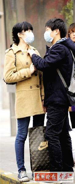 公交站臺(tái)上，一對(duì)年輕人戴著口罩，系緊衣領(lǐng)。